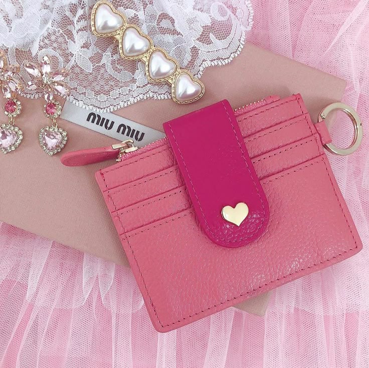 Pink leather cardholder with heart embellishment, lace, and heart jewelry, styled on a Miu Miu background with pink tulle fabric.