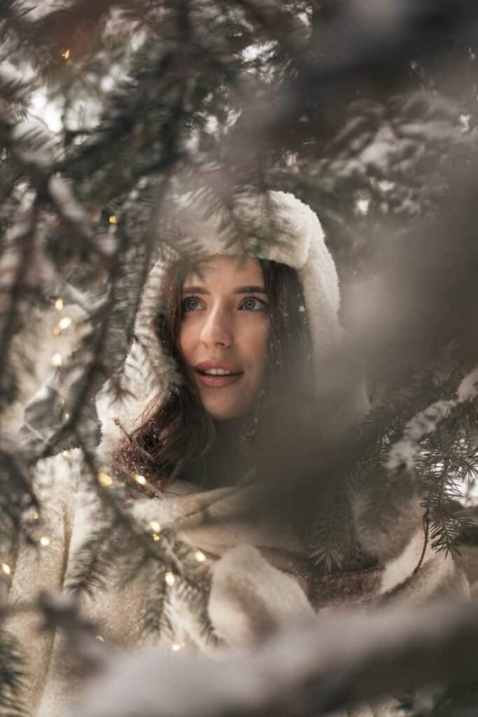 _ - 2025-12-04T130728015 Woman in a cozy winter hood standing among snowy pine branches adorned with warm fairy lights, looking serene and thoughtful. | Sky Rye Design Woman in a cozy winter hood standing among snowy pine branches adorned with warm fairy lights, looking serene and thoughtful.