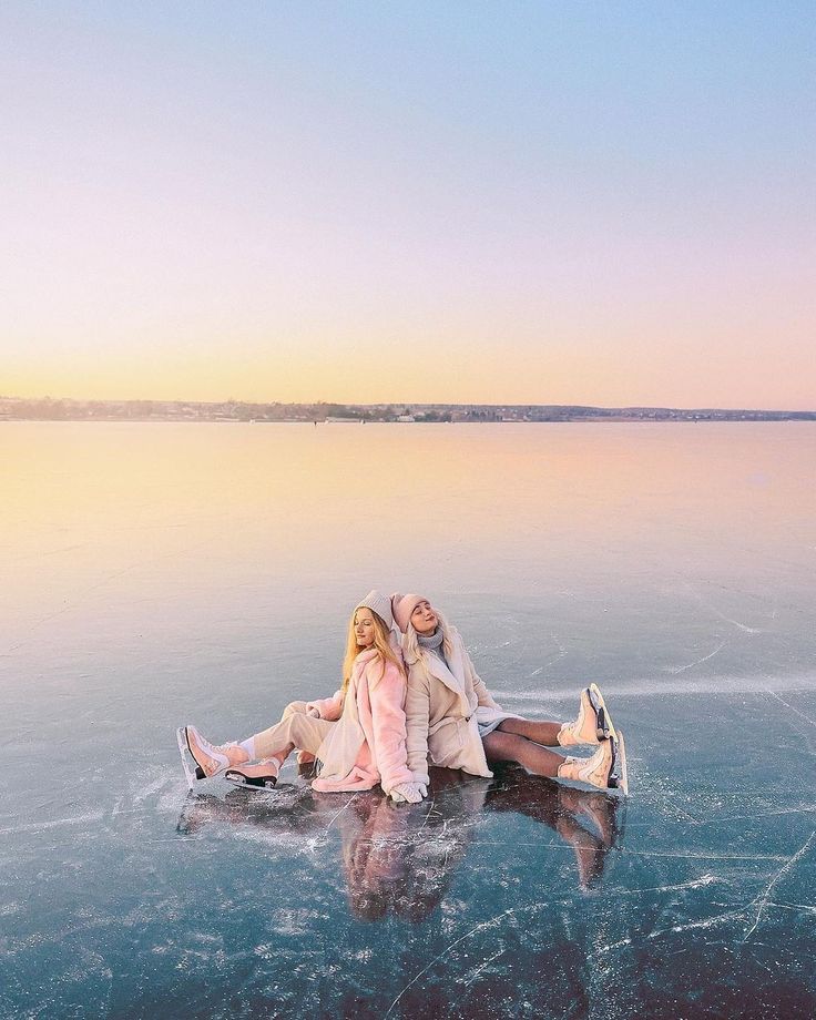 _ - 2025-12-04T130957939 Two women in pastel coats and ice skates sitting on a frozen lake at sunset, reflecting serene winter vibes and scenic beauty. | Sky Rye Design Two women in pastel coats and ice skates sitting on a frozen lake at sunset, reflecting serene winter vibes and scenic beauty.