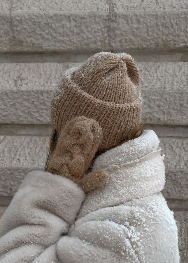 _ - 2025-12-04T132332233 Person bundled in a cozy beige knit hat and gloves with a fluffy white coat, covered in snowflakes, standing by a brick wall. | Sky Rye Design Person bundled in a cozy beige knit hat and gloves with a fluffy white coat, covered in snowflakes, standing by a brick wall.