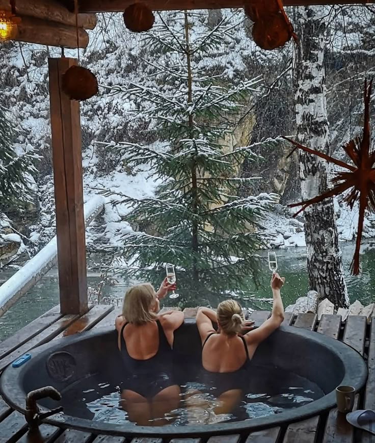 Two people relaxing in a hot tub, toasting with champagne glasses amid a snowy winter landscape, creating a cozy retreat vibe.