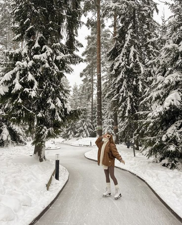 Person ice skating on curvy snow-covered forest path, surrounded by tall, snow-laden trees, wearing winter clothing.