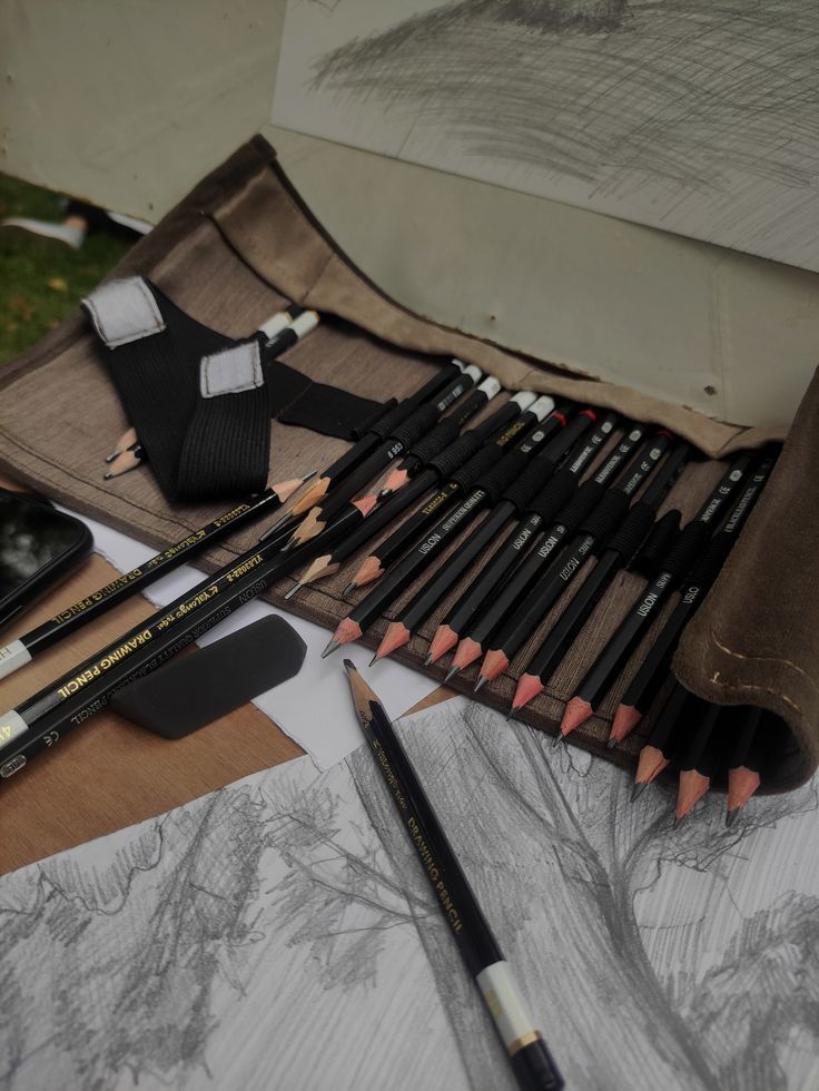 Sketching tools and pencils arranged on a table with detailed nature drawings; perfect setup for an artist's outdoor sketch session.