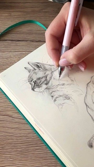 Hand sketching a realistic cat portrait in a notebook on a wooden table. Pen and detailed drawing process highlighted.