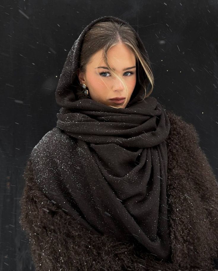 Woman in a cozy brown hooded coat with snowflakes, looking serene against a dark winter background.