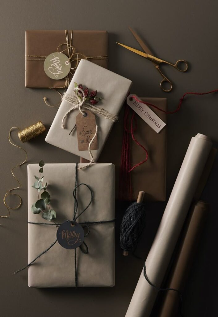 Gift packages with festive wrapping, tags, and decorations. Scissors, twine, and greenery accents create a cozy Christmas vibe.