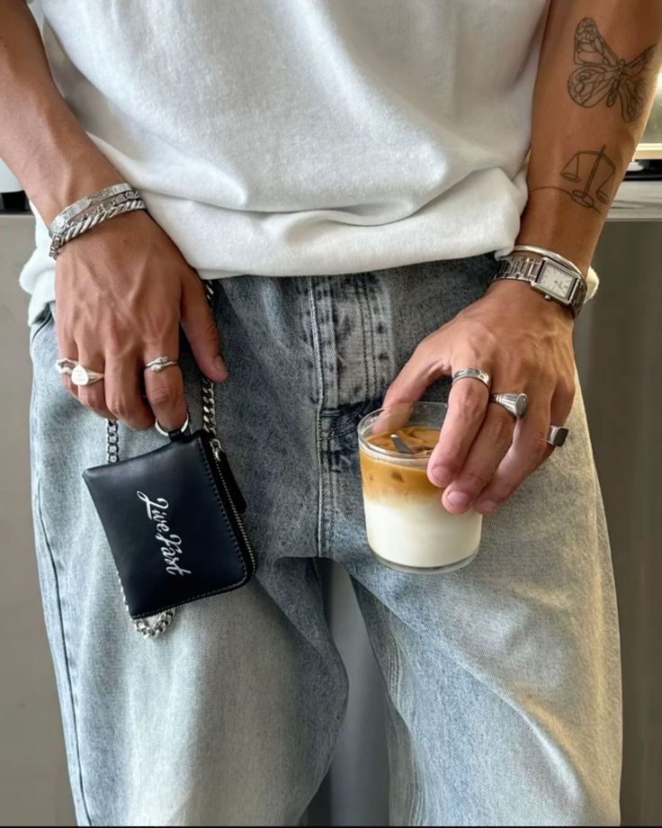 Casual style: person in light jeans holds iced coffee and black wallet, adorned with silver jewelry and tattoos for a trendy look. Top Guys Tattoo Ideas 