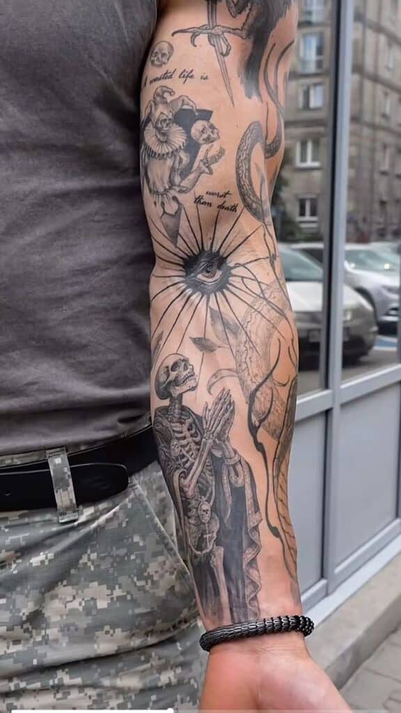 Black and gray sleeve tattoo featuring detailed skeletons, an eye, and artistic elements on a man's arm, reflecting a gothic theme.