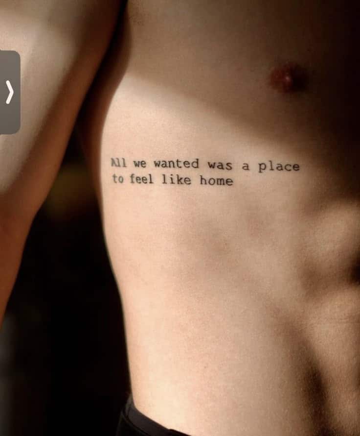 Tattoo on person's side reading All we wanted was a place to feel like home, symbolizing belonging and comfort in minimalist font.