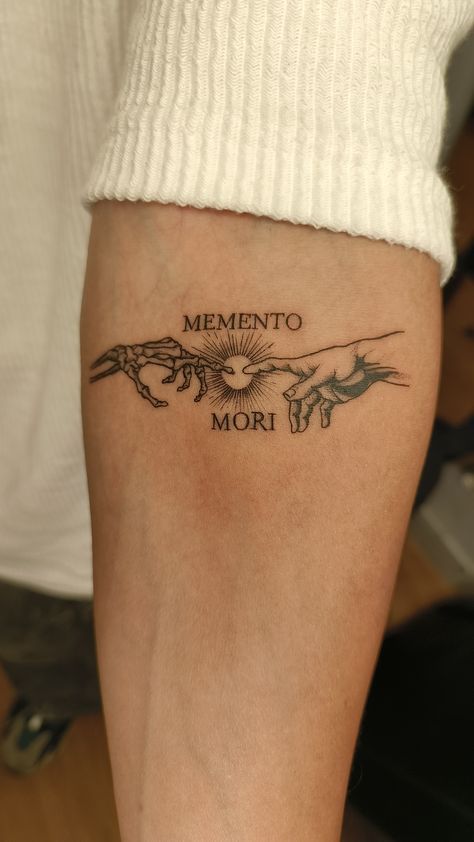 Arm tattoo with Memento Mori text, depicting skeletal and human hands reaching for each other, symbolizing life and mortality theme.