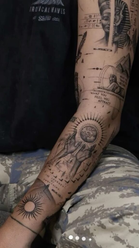 Intricate arm tattoo featuring Egyptian motifs, spiritual symbols, and detailed designs on a person wearing a dark shirt and camo pants.