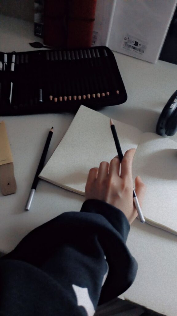 _ - 2025-12-10T114957021 Hand holding a pencil over sketchbook, surrounded by drawing supplies on a desk. Perfect for art, creativity, or study themes. | Sky Rye Design Hand holding a pencil over sketchbook, surrounded by drawing supplies on a desk. Perfect for art, creativity, or study themes.