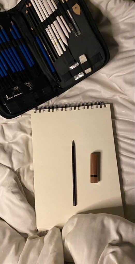 _ - 2025-12-10T115005429 Art supplies on a bed: open sketchbook with a pencil and sharpener, accompanied by a case filled with various drawing tools. | Sky Rye Design Art supplies on a bed: open sketchbook with a pencil and sharpener, accompanied by a case filled with various drawing tools.
