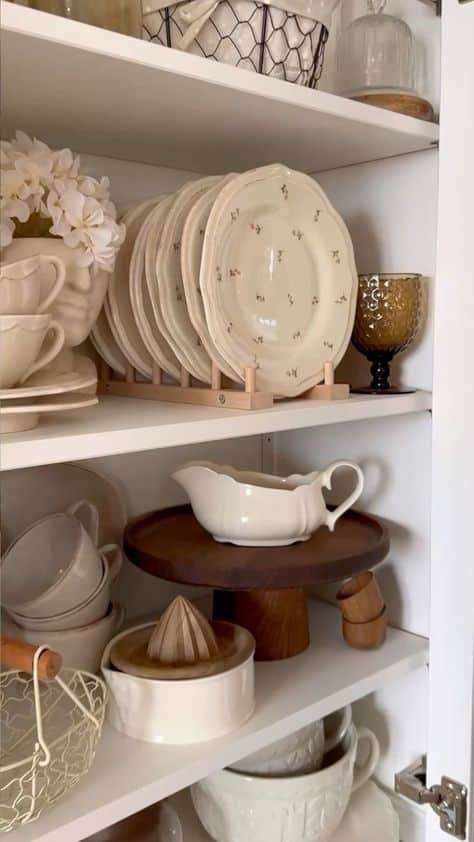 _ - 2025-12-10T134341687 Neatly organized kitchen shelves with ceramic plates, mugs, and vases, featuring a decorative touch with flowers and an amber glass. | Sky Rye Design Neatly organized kitchen shelves with ceramic plates, mugs, and vases, featuring a decorative touch with flowers and an amber glass.