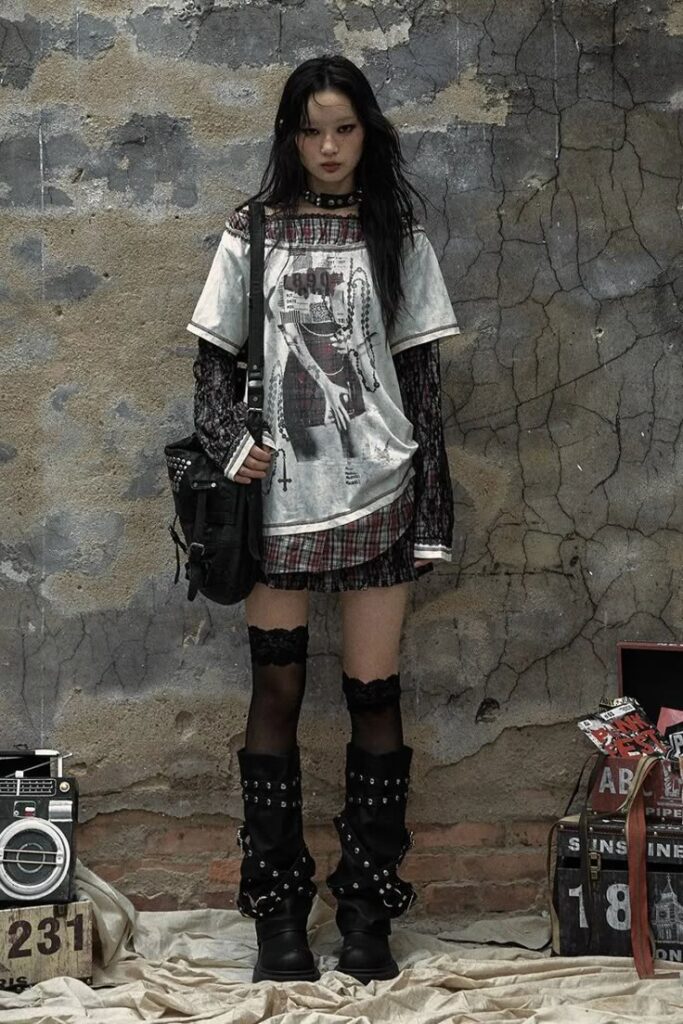 Grunge-inspired fashion with layered clothing, studded boots, and edgy accessories in front of a textured, urban backdrop.