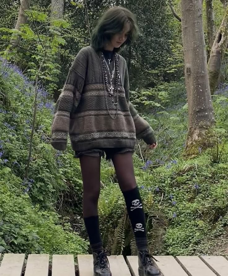 Person in a cozy oversized sweater and skull socks walking on a wooden path in a lush green forest setting.