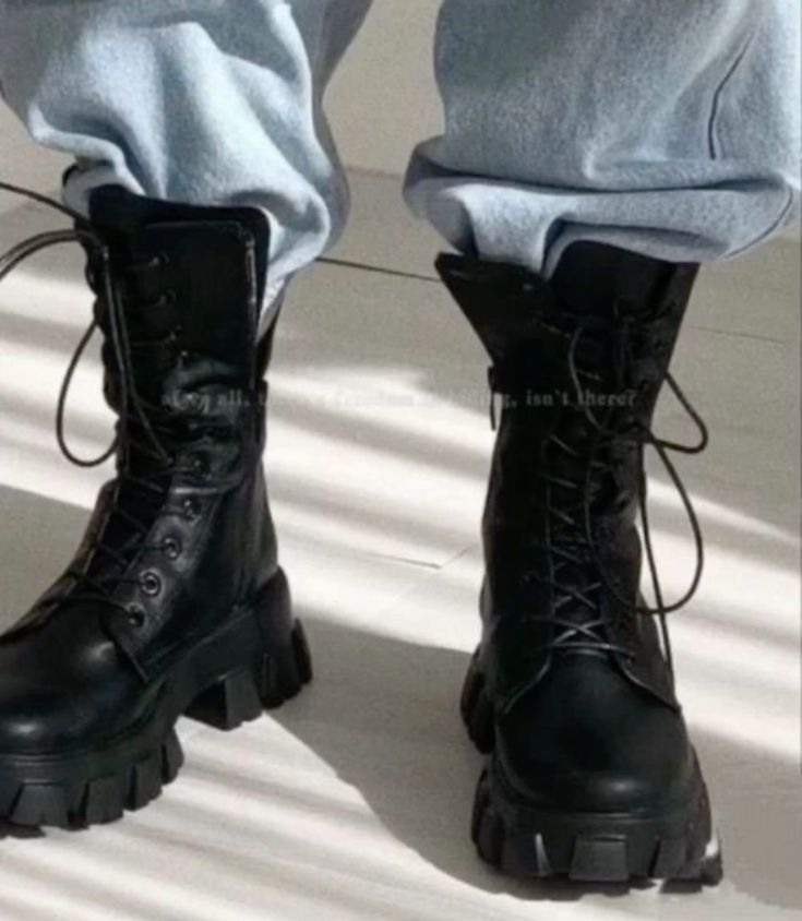 Black combat boots with chunky soles paired with rolled-up light blue jeans, styled for a modern, rugged look.