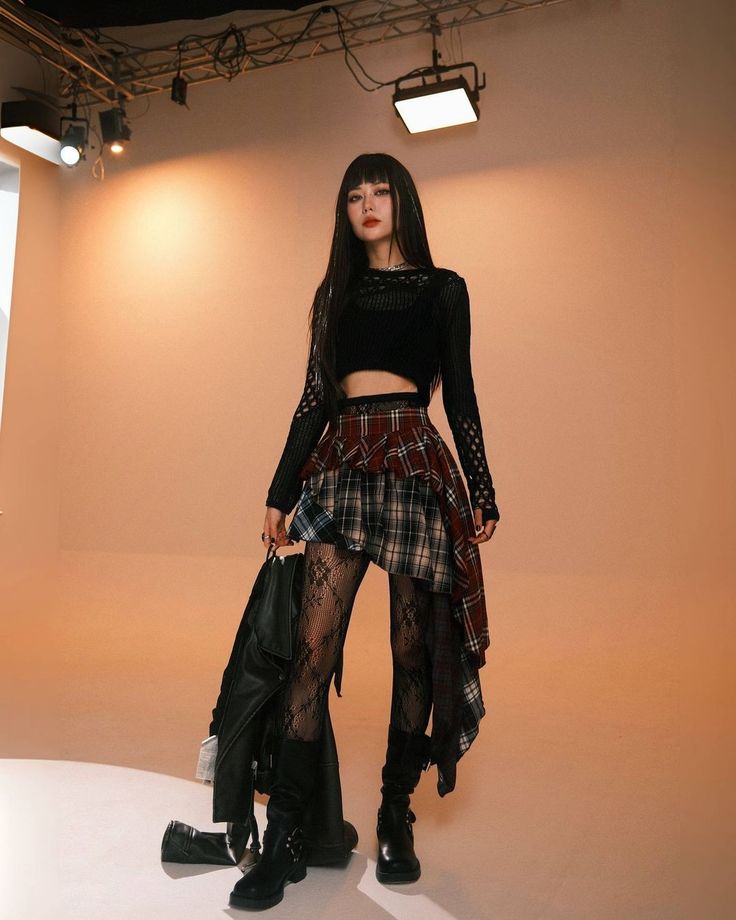 Fashion model in a stylish black top, plaid skirt, lace leggings, and boots on a photoshoot set with bright lighting. Trendy and edgy look.