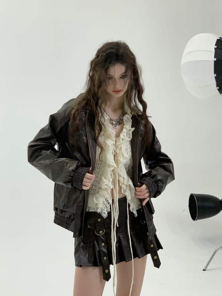 Fashion model in leather jacket and lace top posing in studio with lighting equipment, edgy style.