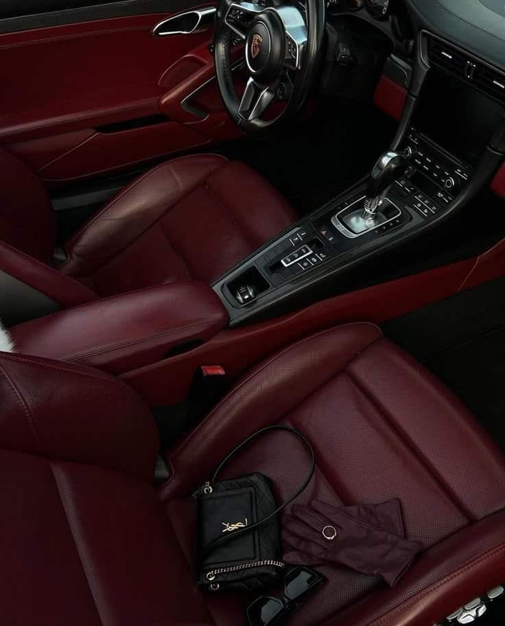 Luxurious red leather car interior with a designer purse, gloves, and sunglasses on the seat, showcasing style and elegance.