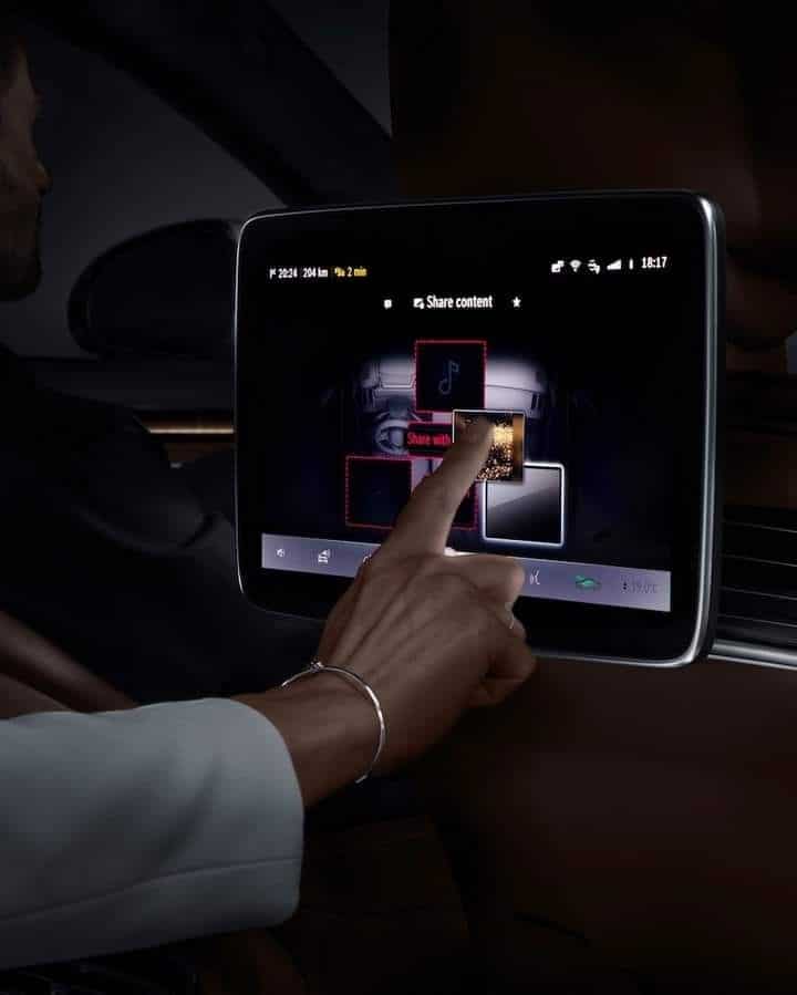 Person interacting with a car's touchscreen display to share content, highlighting in-car technology and connectivity features.