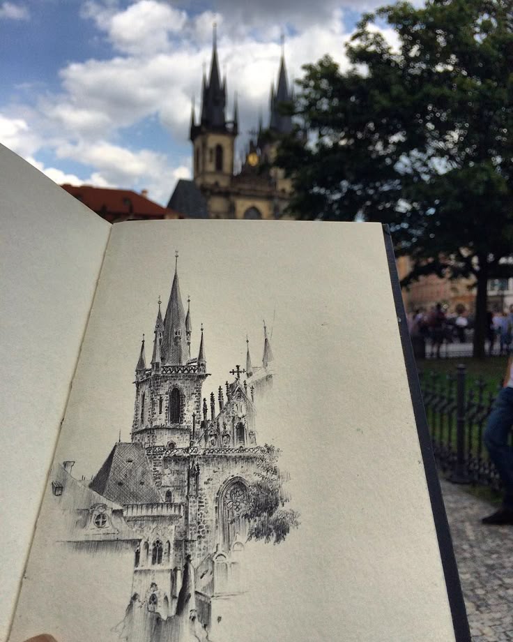_ - 2025-12-12T012310022 Sketch of a historic European cathedral in a notebook, held up against a real cathedral background, highlighting artistic inspiration. | Sky Rye Design Sketch of a historic European cathedral in a notebook, held up against a real cathedral background, highlighting artistic inspiration.