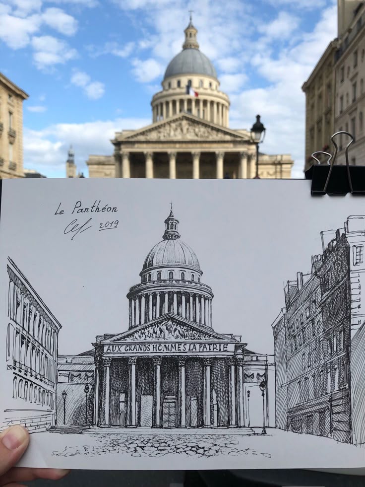_ - 2025-12-12T013237981 Drawing of the Panthéon in Paris held in front of the actual building, showcasing architectural details and artistic interpretation. | Sky Rye Design Drawing of the Panthéon in Paris held in front of the actual building, showcasing architectural details and artistic interpretation.