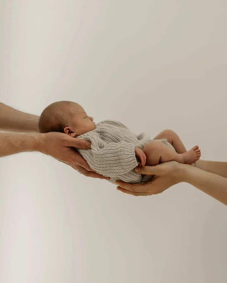 _ - 2025-12-12T124054531 Newborn baby cradled in adult hands, symbolizing care and protection. Warm, minimalist background enhances focus on tender moment. | Sky Rye Design Newborn baby cradled in adult hands, symbolizing care and protection. Warm, minimalist background enhances focus on tender moment.