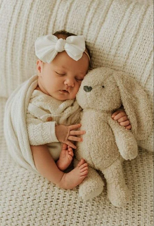 _ - 2025-12-12T131700470 Sleeping baby with a white bow, cuddling a soft bunny toy on a beige blanket, creating a cozy and serene scene. | Sky Rye Design Sleeping baby with a white bow, cuddling a soft bunny toy on a beige blanket, creating a cozy and serene scene.