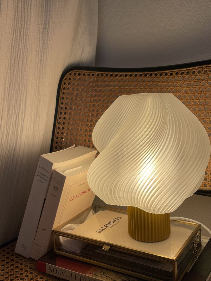 Modern sculpted table lamp illuminating books on a cozy rattan surface, creating a warm and stylish ambiance in a minimalist setting.