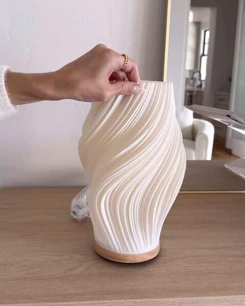 _ - 2025-12-16T234614368 Elegant white vase with textured wave design on wood table, hand adjusting position for decor arrangement. | Sky Rye Design Elegant white vase with textured wave design on wood table, hand adjusting position for decor arrangement.