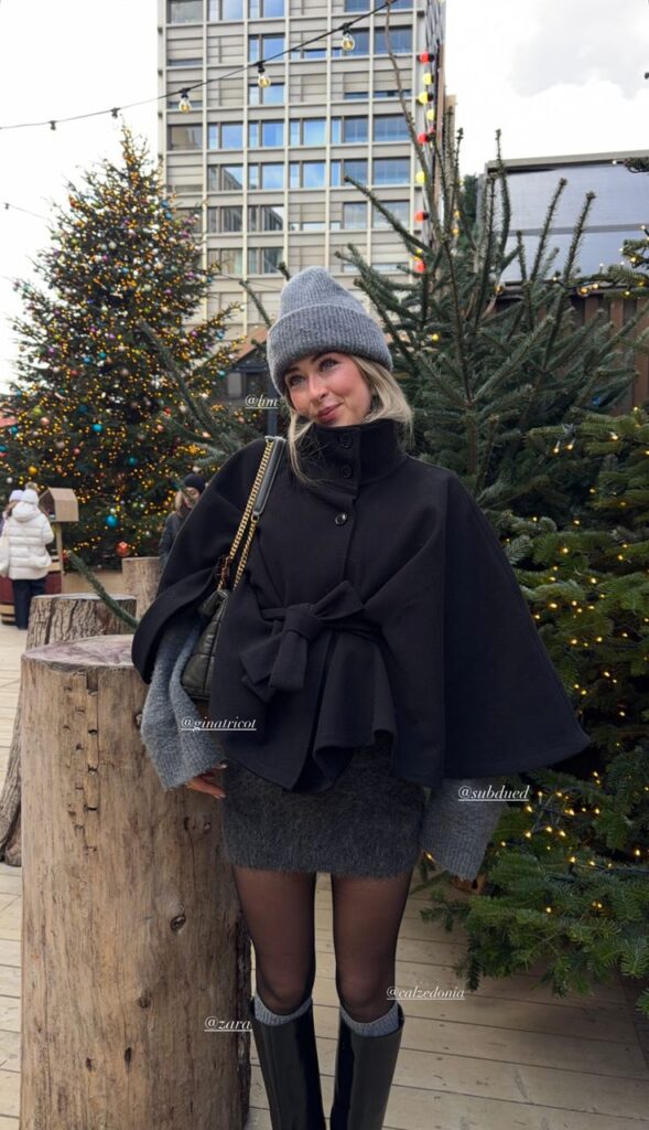 _ - 2025-12-28T122752823 Woman in winter attire posing at a festive outdoor setting with Christmas trees and lights in the background. | Sky Rye Design Woman in winter attire posing at a festive outdoor setting with Christmas trees and lights in the background.