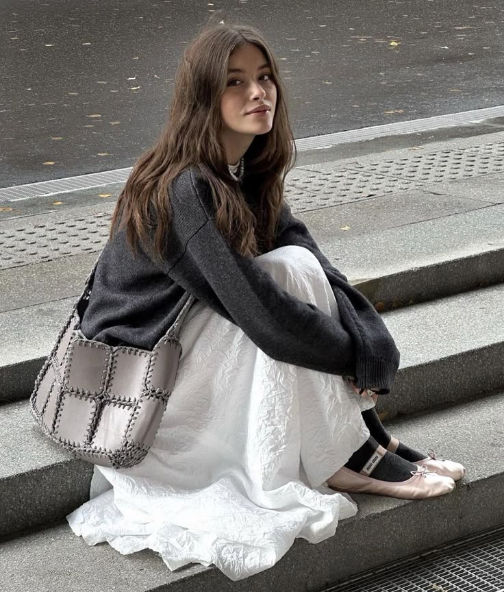 _ - 2025-12-28T125611657 Woman sitting on steps in stylish outfit: gray sweater, white skirt, pink flats, and a chic handbag, with a street background. | Sky Rye Design Woman sitting on steps in stylish outfit: gray sweater, white skirt, pink flats, and a chic handbag, with a street background.