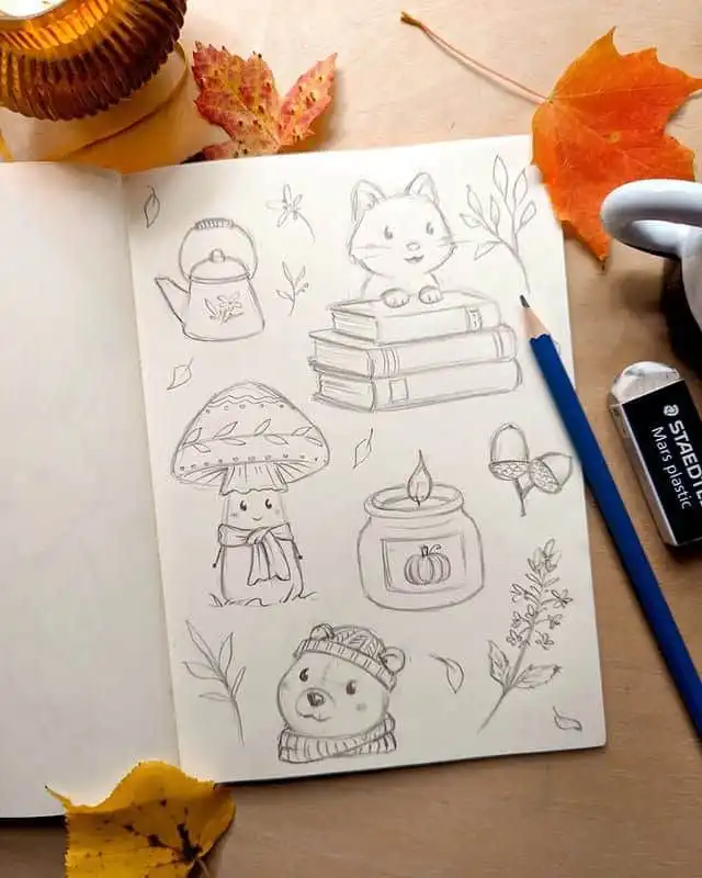 Sketchbook with autumn-themed pencil drawings, including a fox, mushroom, bear, kettle, and leaves, surrounded by colorful fall leaves.