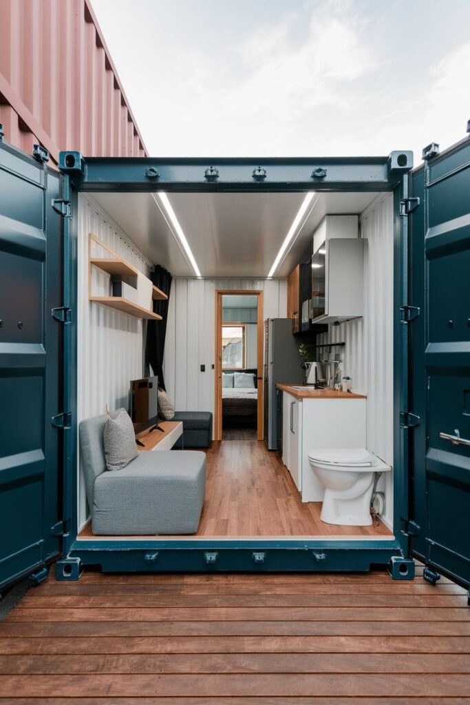 Tiny home interior in a shipping container with modern design, kitchenette, and cozy seating area for compact living.