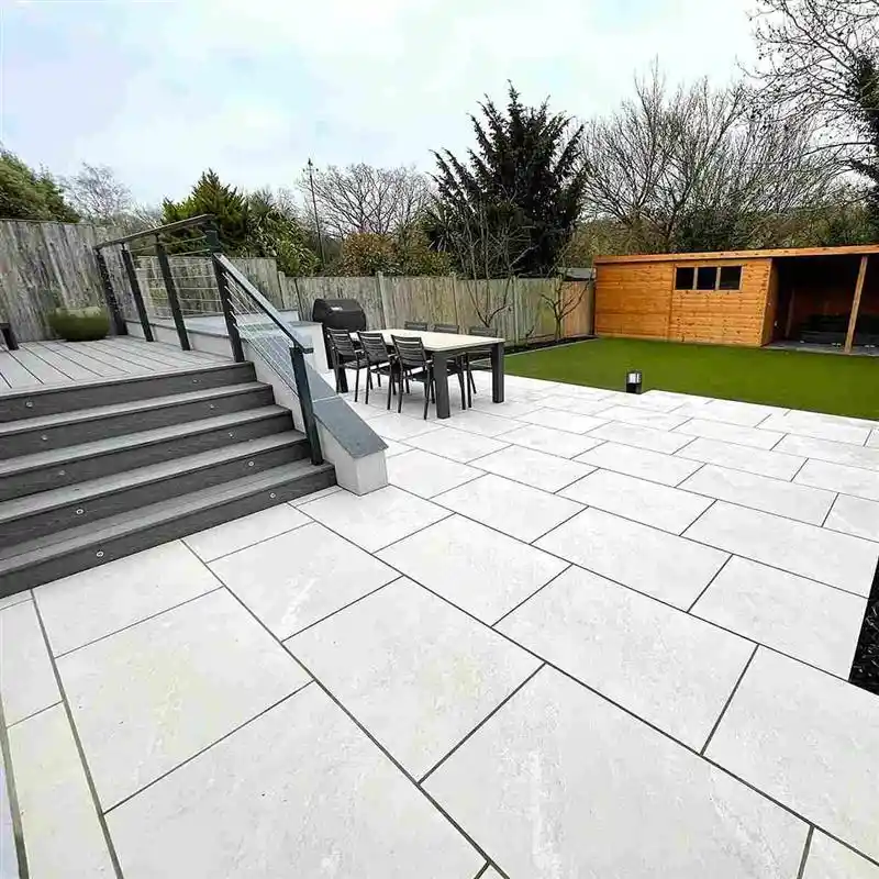 20mm-porcelain-slabs-for-patios-avoid-installation-mistakes Modern backyard patio with sleek white tiles, outdoor dining set, wooden shed, and lush lawn, surrounded by a wooden fence and trees. | Sky Rye Design Modern backyard patio with sleek white tiles, outdoor dining set, wooden shed, and lush lawn, surrounded by a wooden fence and trees.
