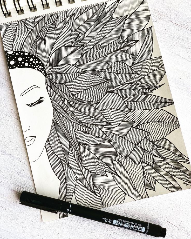 Intricate black ink drawing of a woman's profile with detailed leaf-like hair, beside a black pen on a textured white surface.