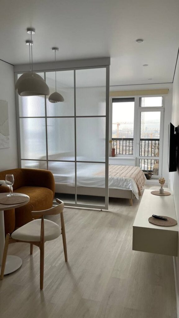_ 21 Modern studio apartment with cozy furnishings, large window view, stylish partition, and warm lighting. Ideal for minimalist living. | Sky Rye Design Modern studio apartment with cozy furnishings, large window view, stylish partition, and warm lighting. Ideal for minimalist living.