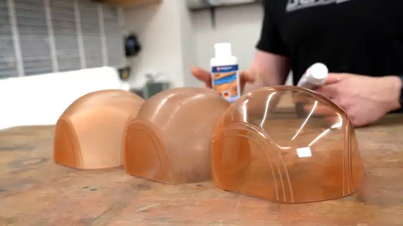 Clear plastic domes on a workbench with a person holding a bottle in the background, showcasing crafting materials in a workshop.