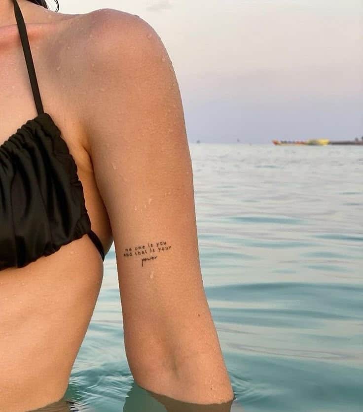 Person in black swimsuit with arm tattoo in ocean, highlighting uniqueness and empowerment.