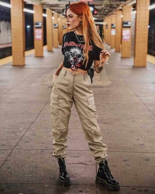 _ 22 Trendy woman in a graphic tee and cargo pants stands confidently on a subway platform, showcasing alternative fashion style. | Sky Rye Design Trendy woman in a graphic tee and cargo pants stands confidently on a subway platform, showcasing alternative fashion style.