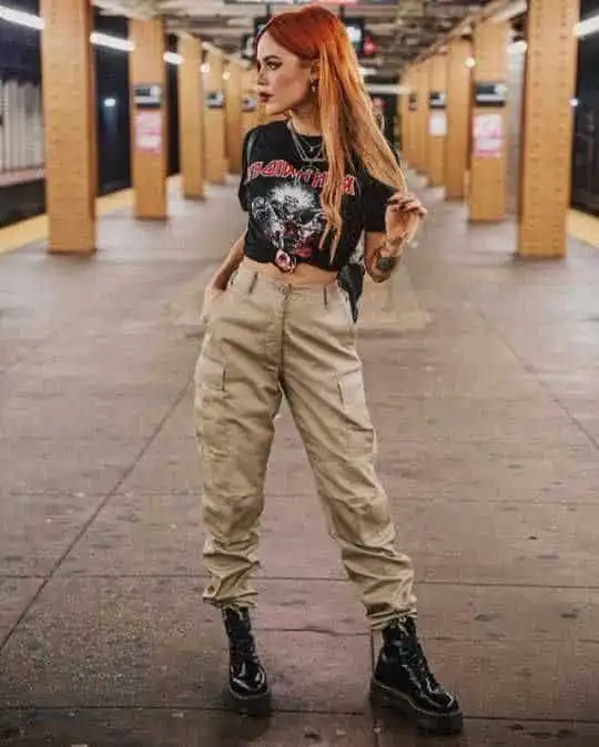 Trendy woman in a graphic tee and cargo pants stands confidently on a subway platform, showcasing alternative fashion style.