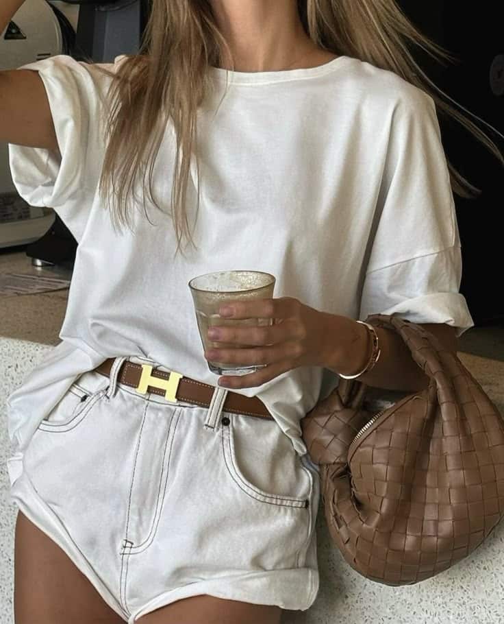 _ 22 Woman in white t-shirt and shorts holding a drink, with a brown bag on her arm. Casual summer fashion with stylish belt and accessories. | Sky Rye Design Woman in white t-shirt and shorts holding a drink, with a brown bag on her arm. Casual summer fashion with stylish belt and accessories.
