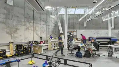 Robotics lab with students collaborating on projects, surrounded by equipment and a testing area with colorful parts and tools.