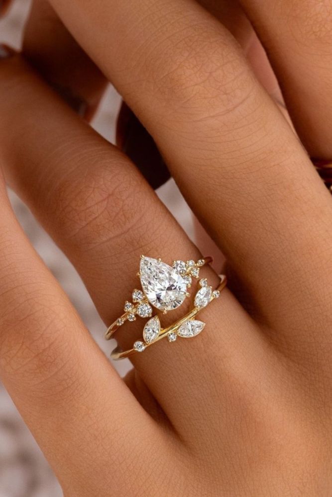 226dcfa01e0783eb56b9626b8e3258f9 Elegant gold and diamond engagement ring set on a woman's finger, featuring a pear-shaped gemstone and delicate floral accents. | Sky Rye Design Elegant gold and diamond engagement ring set on a woman's finger, featuring a pear-shaped gemstone and delicate floral accents.