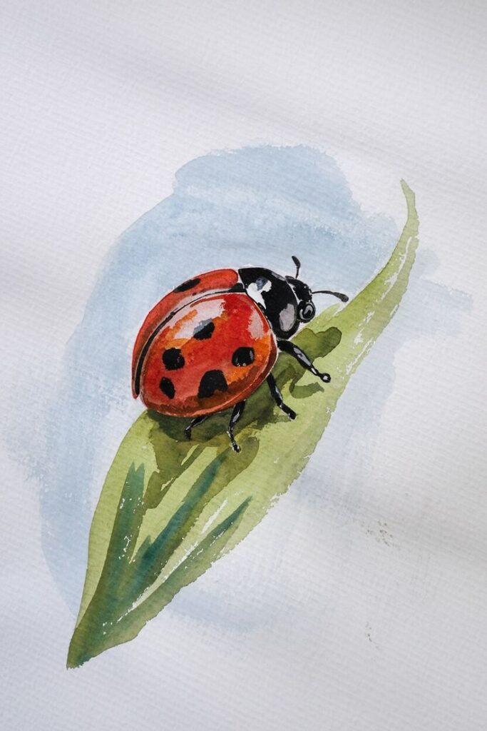 Watercolor painting of a red and black ladybug on a green leaf, featuring detailed textures and soft blue background.