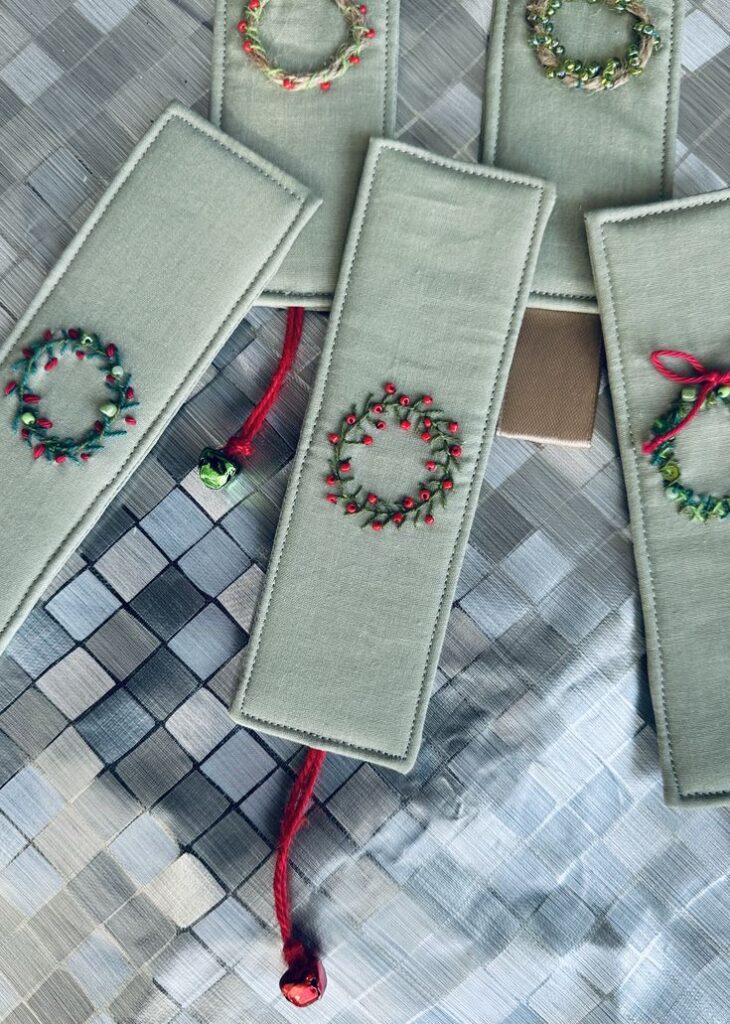 _ 28 Green handmade bookmarks with red and green embroidery, set on a textured surface. | Sky Rye Design Green handmade bookmarks with red and green embroidery, set on a textured surface.