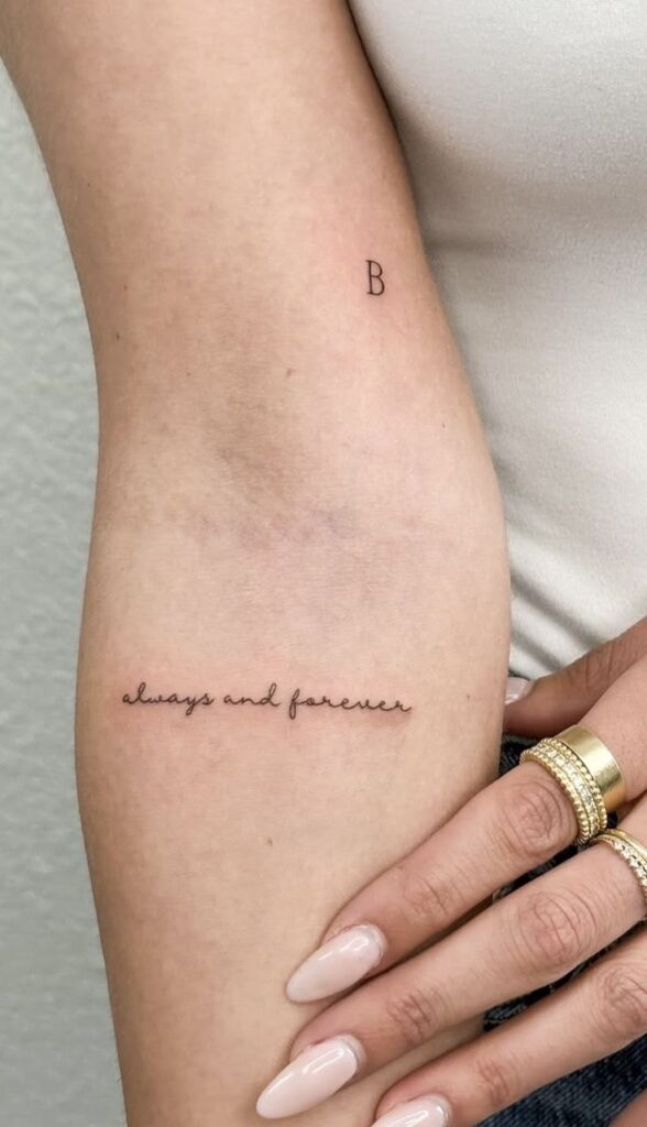 Minimalist always and forever arm tattoo with cursive script and initial B. Stylish gold rings and nude nails.