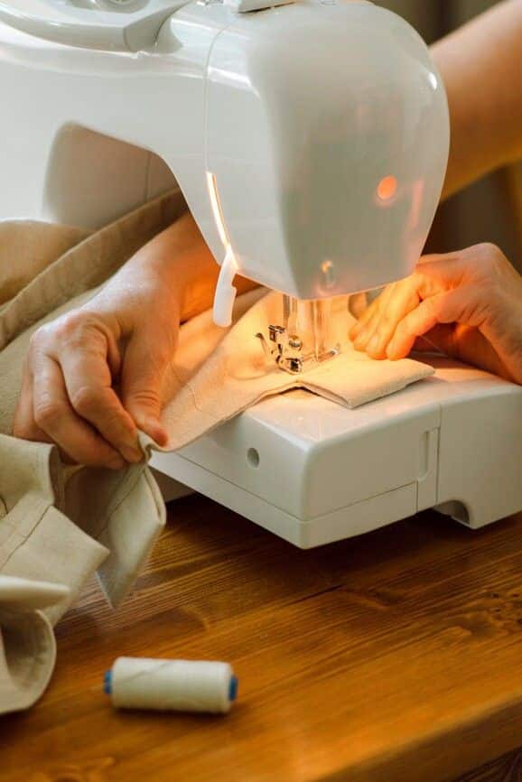 _ 3 Person sewing on a white sewing machine, fabric in hand, with soft lighting. Perfect for DIY, crafts, or sewing tutorials. | Sky Rye Design Person sewing on a white sewing machine, fabric in hand, with soft lighting. Perfect for DIY, crafts, or sewing tutorials.