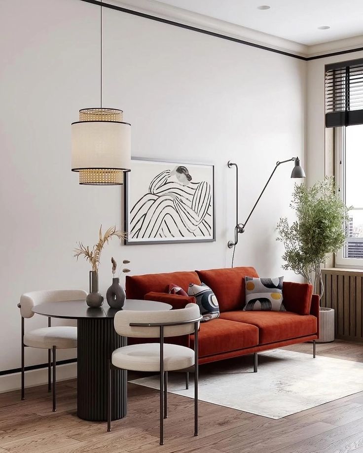Modern living room with orange sofa, abstract art, round dining table, stylish chairs, and a potted plant by the window.